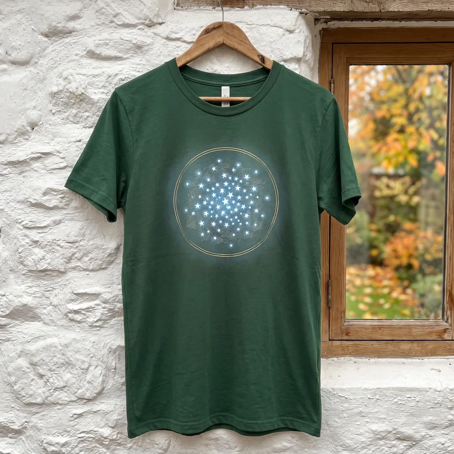 The forest green Seven Sisters tee on a wooden hanger against a whitewashed cottage wall